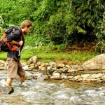 vecteezy_young-white-man-with-backpack-crosses-the-mountain-river_15048885