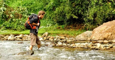 vecteezy_young-white-man-with-backpack-crosses-the-mountain-river_15048885