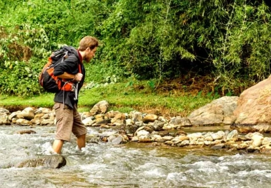 vecteezy_young-white-man-with-backpack-crosses-the-mountain-river_15048885