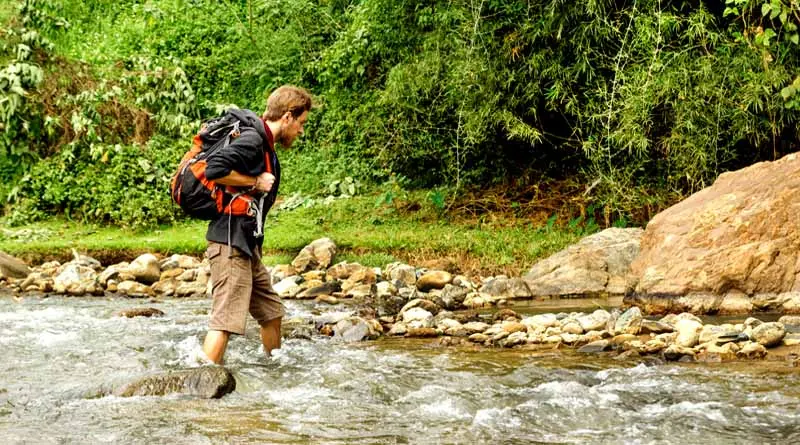 vecteezy_young-white-man-with-backpack-crosses-the-mountain-river_15048885